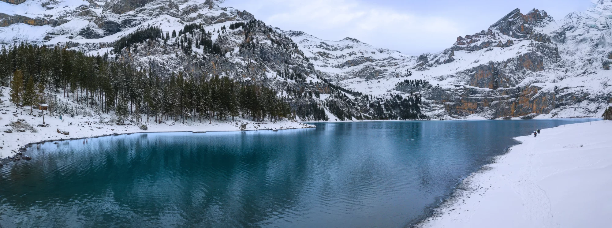 Lac alpin enneigé avec forêts et falaises, panorama hivernal