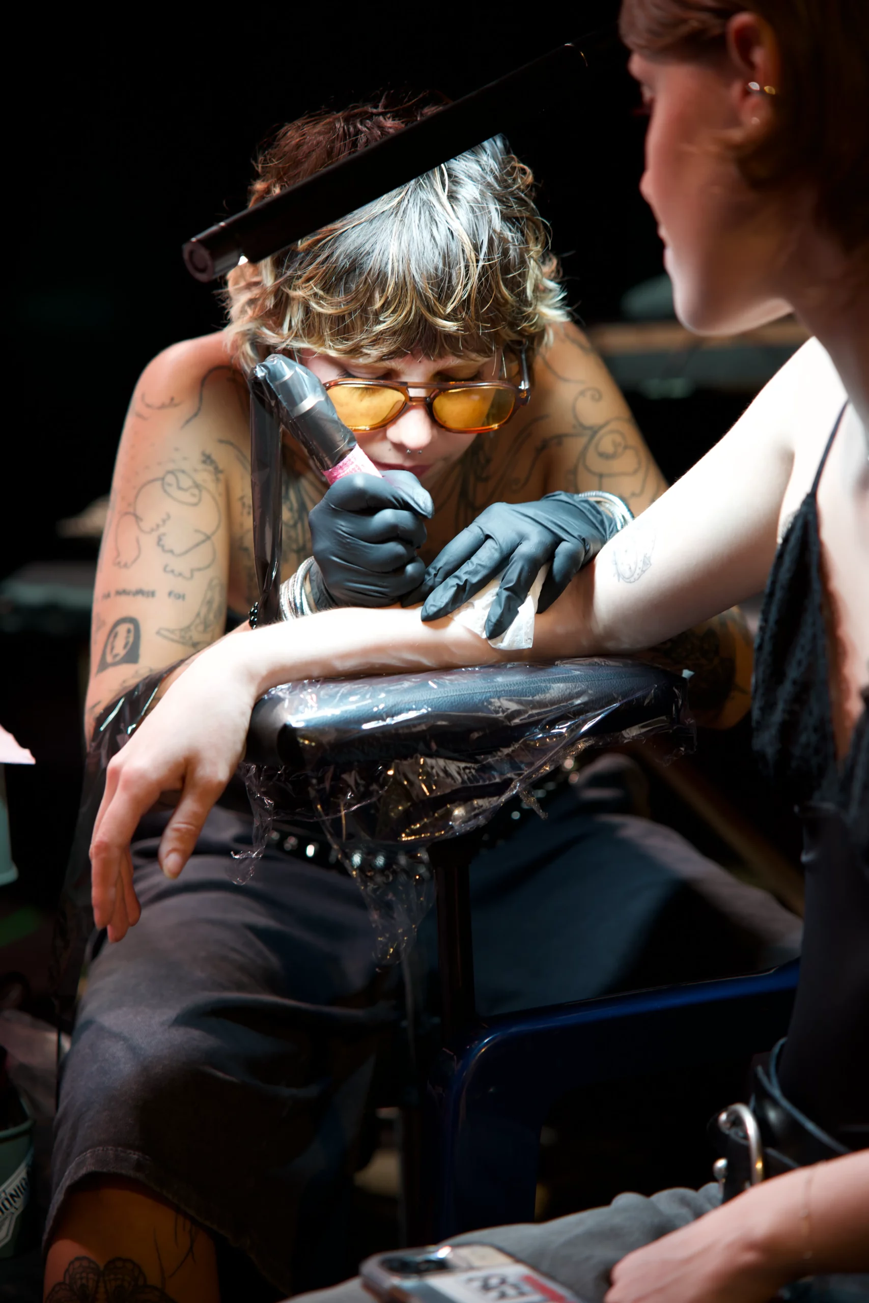 Femme tatouage bras artiste encrage studio sombre intense, photographie portrait tattoo artistique passionné.