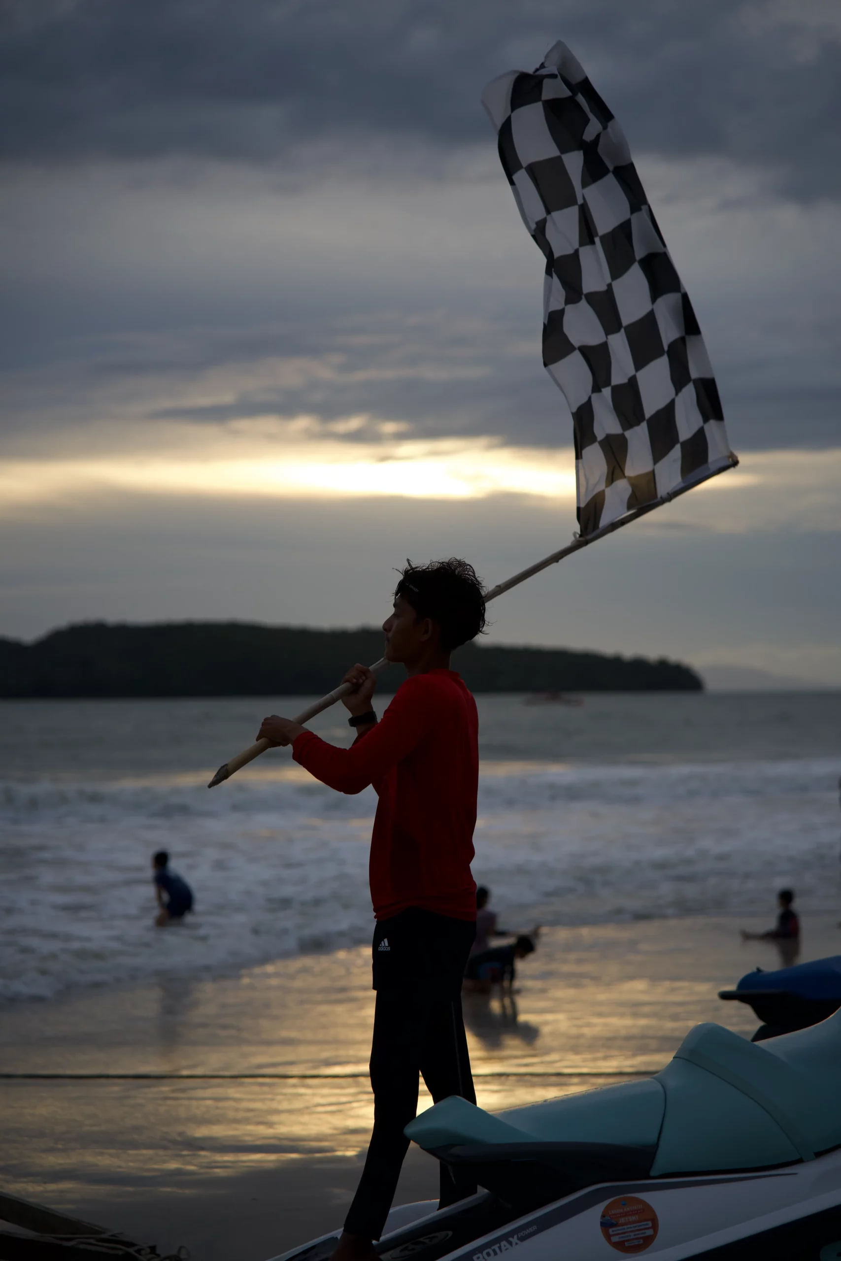 Homme drapeau à damier plage sunset jet-skis silhouettes, objectif standard action sportive émotionnelle.