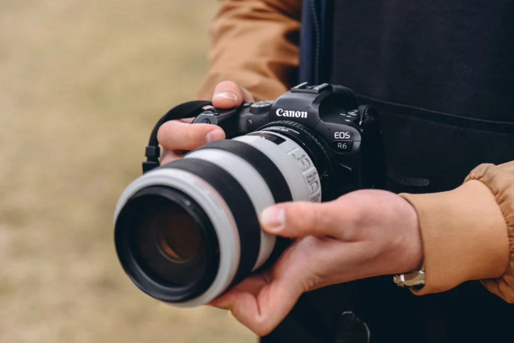 Photographe tenant un Canon EOS R6 avec téléobjectif blanc en extérieur.