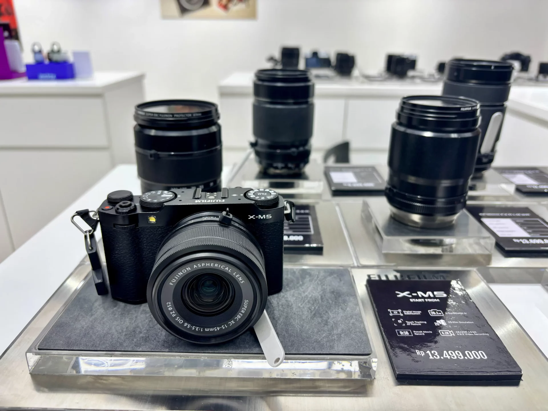 Fujifilm X-M5 avec objectif en magasin photo entouré d’objectifs, nouvel hybride Fujifilm polyvalent.